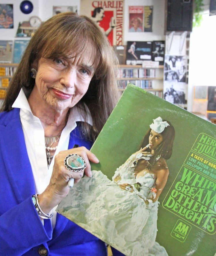Dolores Erickson smiling while holding the album cover of Whipped Cream & Other Delights by Herb Alpert's Tijuana Brass