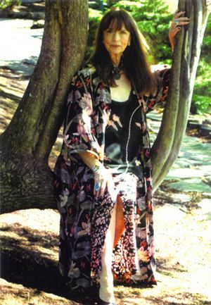 Dolores Erickson smiling while sitting on a branch of tree and wearing a floral dress