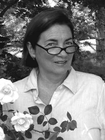 Dolores Hayden smiling with a flower on her side while wearing a blouse and eyeglasses