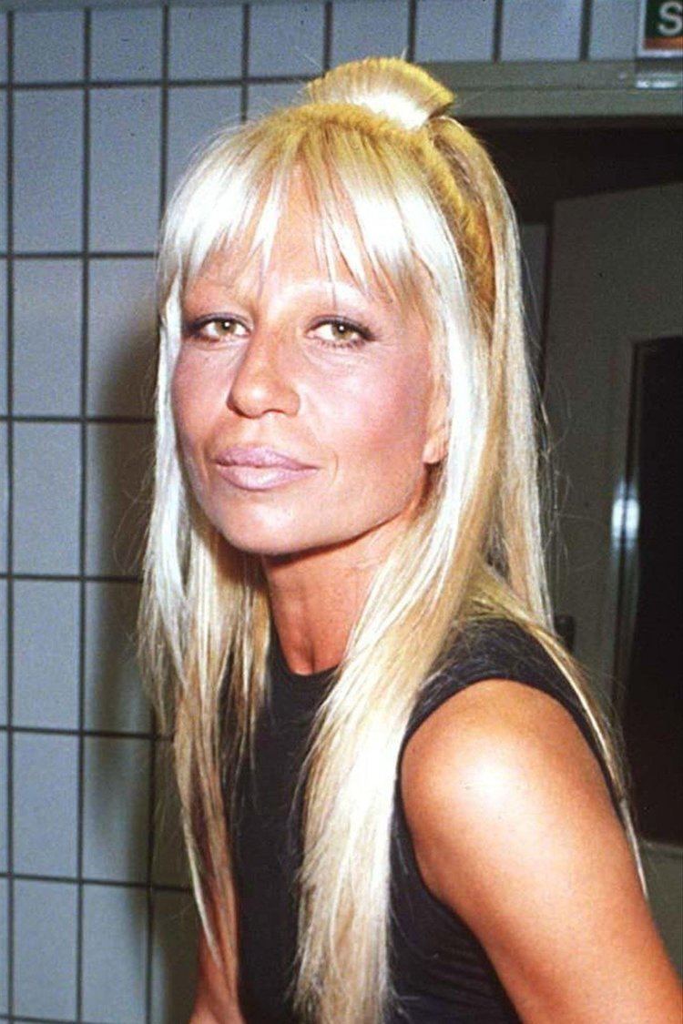 Donatella Versace smiling with a blonde hair and wearing a black dress