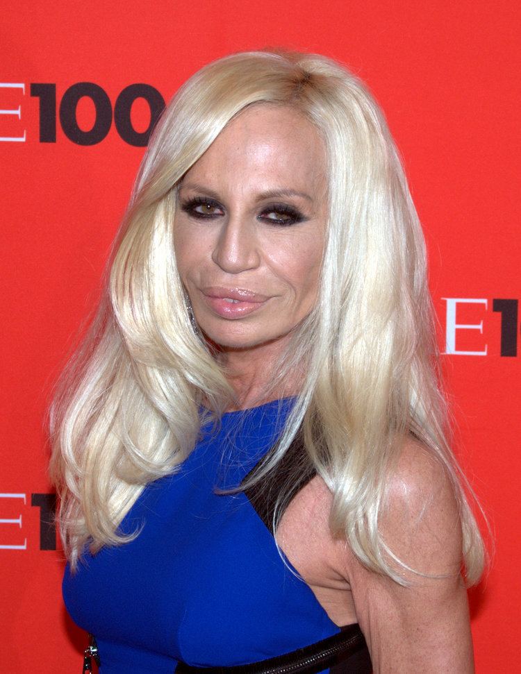 Donatella Versace smiling with a wavy blonde hair and wearing a blue dress