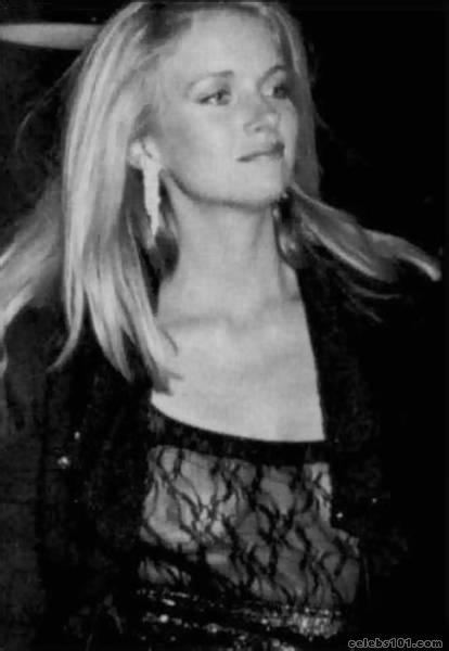 Donna Dixon smiling with straight blonde hair while wearing a sexy black dress and earrings