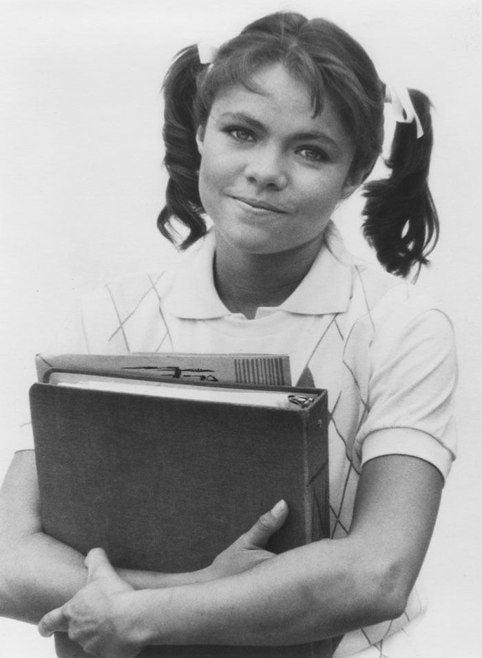 Donna Wilkes smiling with her hair bunched and holding a book while wearing a white striped shirt.