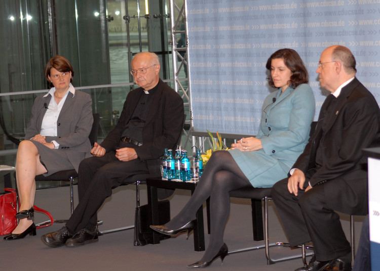 Dorothee Bär sitting on the chair with two men and a woman while wearing blue long sleeve dress, black heels, and black pantyhose