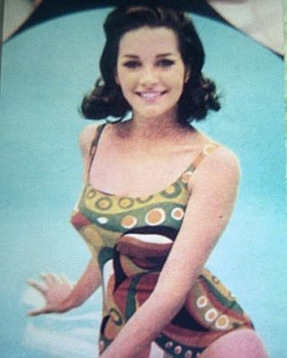 Miss USA 1968 Dorothy Anstett smiling, with wavy black hair, and wearing a multi-colored one-piece swimsuit.