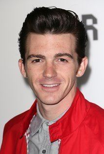 Drake Bell Dsmiling while wearing a gray shirt under a red coat