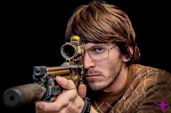 Dugan Ashley wearing a brown jacket while aiming his gun