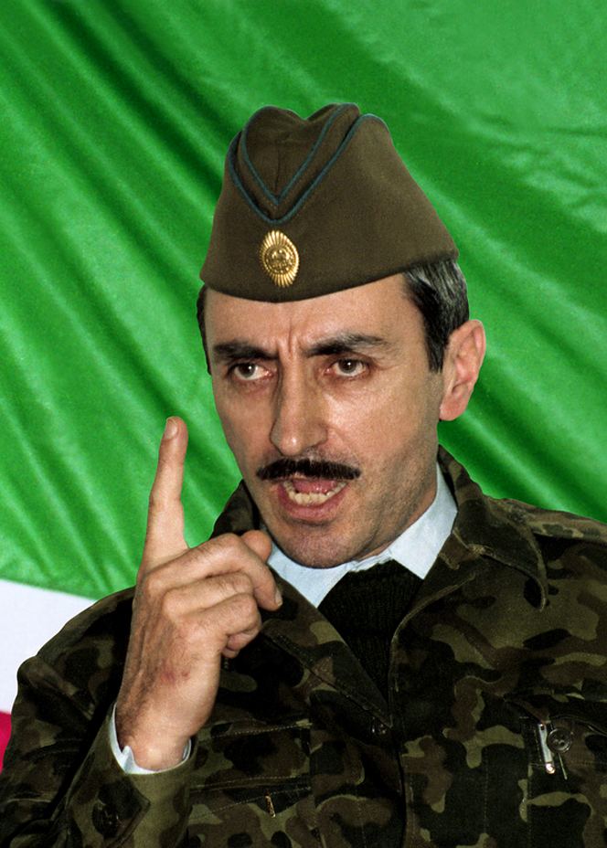 Dzhokhar Dudayev pointing his finger up, with an angry face and mustache with a green cloth in his background, while wearing a brownish-green side cap with a gold pin and a white long sleeve under a black sweater and camouflage jacket