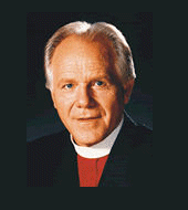 Earl Paulk smiles while wearing a red and white shirt and a black coat