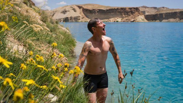 Eddie Ayres looking happy from swimming in a lake while wearing shorts and topless with tattoos on both arms