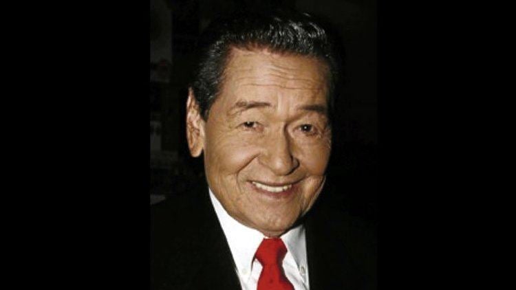 Eddie Garcia smiling while wearing a black coat, white long sleeves, and red necktie