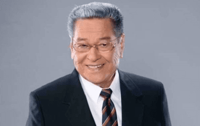 Eddie Garcia smiling while wearing eyeglasses, black coat, white long sleeves, and black and red striped necktie