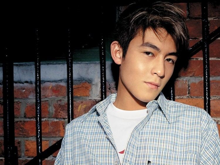 Edison Chen smiling while leaning on the bars and wearing a white shirt under a blue plaid sleeves