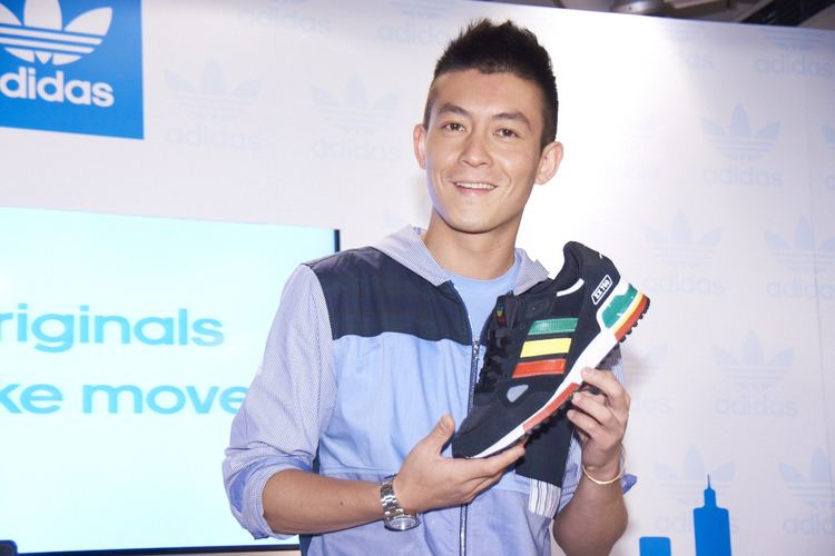 Edison Chen smiling while holding and wearing a blue shirt