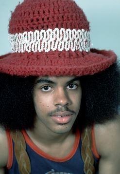 Edmund Sylvers smiling, with kinky hair, wearing a white and red knitted hat, and a brown, red and blue sleeveless shirt.