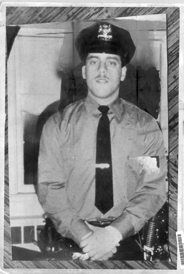 Edward Byrne smiling, wearing a black police cap, long sleeves, and a black necktie.