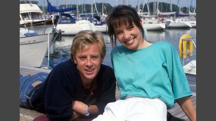 Edward Highmore smiling and wearing black long sleeves and denim pants while Cindy Shelley wearing a sky-blue t-shirt