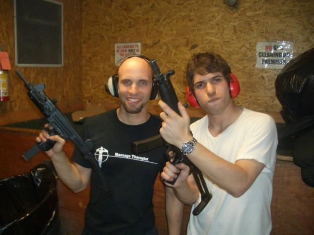 David Packouz and Efraim Diveroli smiling while carrying guns and wearing shooting earmuffs at a gun range near Miami.