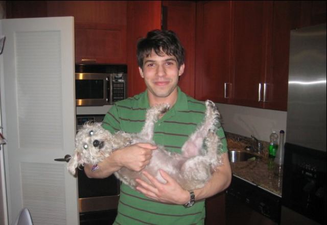 Efraim Diveroli smiling while carrying a dog and wearing a black and green striped shirt