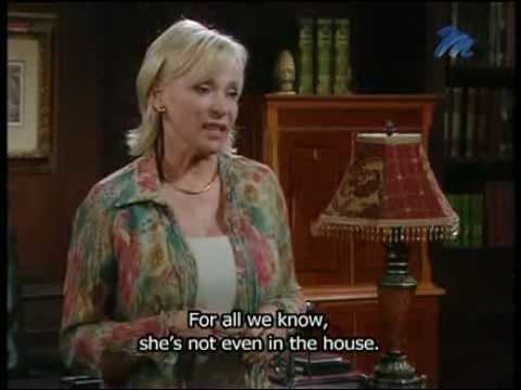 Brümilda van Rensburg talking to someone while wearing a green and pink floral blouse and white inner blouse in a scene from the 1992  soap opera, Egoli: Place of Gold