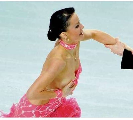 Ekaterina Rubleva is smiling while doing ice dancing and covering her right breast while holding a man's hand, wearing earrings, a necklace, and a pink choker and dress.