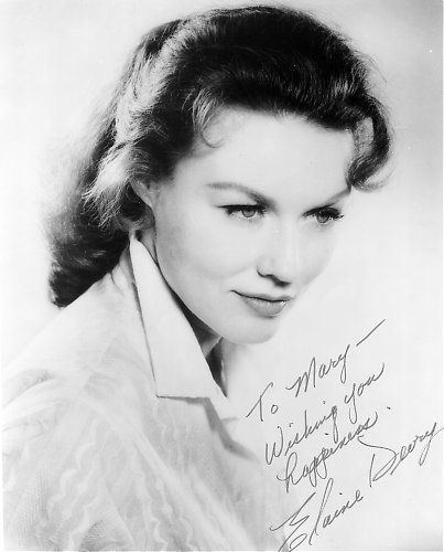 A picture of Elaine Devry wearing a white shirt with her autograph.