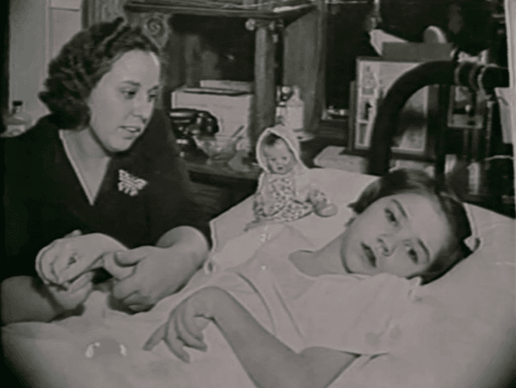 Elaine Esposito lying on a bed while her mom Lucy Esposito holding her hand