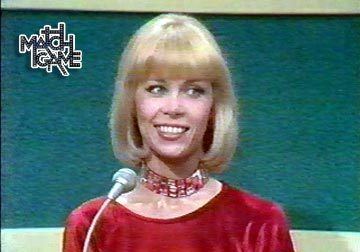 Elaine Joyce smiling during the Match Game Comedy's game show while wearing a red blouse and red chocker