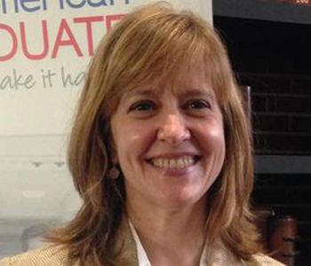 Eleanor Beardsley smiling with shoulder-length golden-blonde hair while wearing earrings and a white blouse under a beige coat