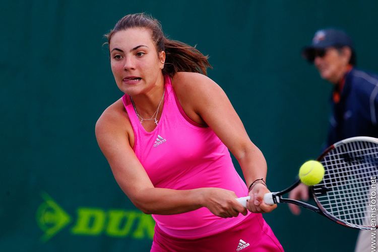 Elena Gabriela playing tennis while wearing a pink top, pink skirt and necklace