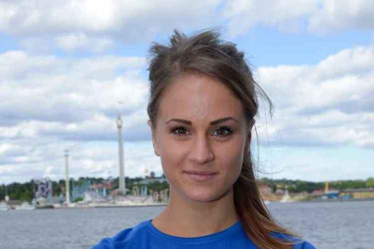 Elin Westerlund smiling in a ponytail with the sea and infrastructures in the background while wearing a blue shirt
