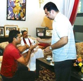 Dr. Eliyantha White giving medications to Sachin Tendulkar who is sitting on the couch and wearing a red t-shirt