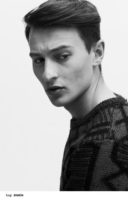 Elliott Tittensor with a serious face while looking at his side and wearing a black knitted sweatshirt.