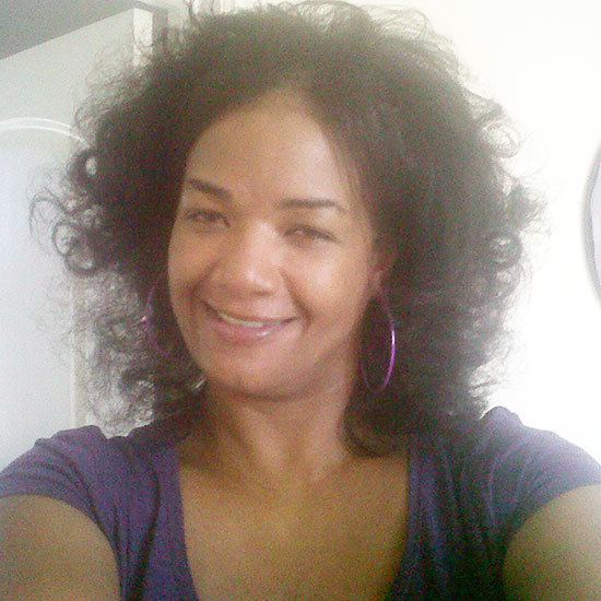 Elvira Wayans smiling while wearing a violet t-shirt and earrings
