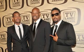Marlon Wayans, Keenen Ivory Wayans, and Shawn Wayans smiling while wearing a black coat, white long sleeves, and black necktie
