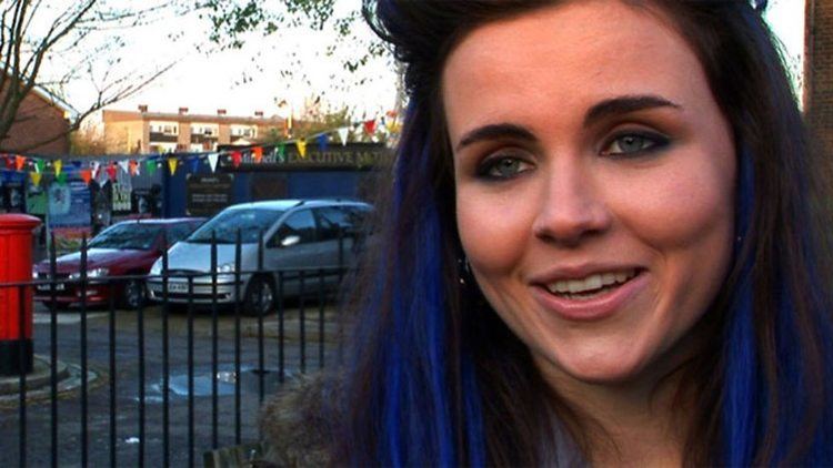 Emer Kenny smiling while in the parking lot and with black and blue color hair.