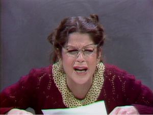Gilda Radner as Emily Litella crying while wearing a red crochet blazer, polka dot blouse, and eyeglasses at the Saturday Night Live