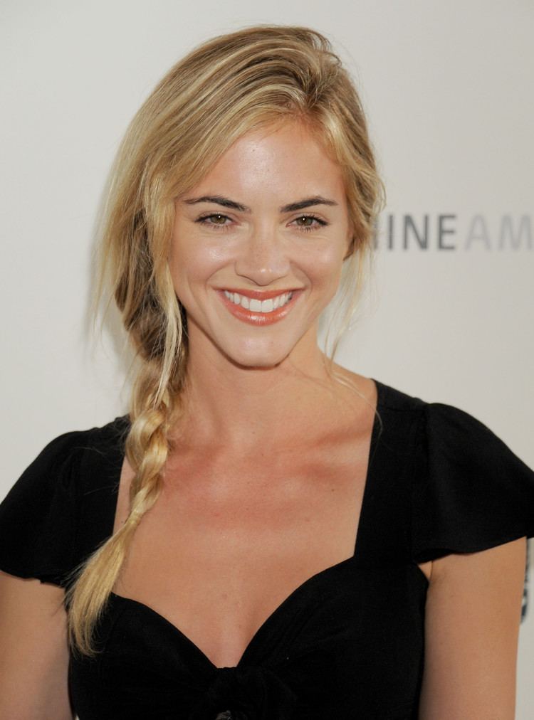 Emily Wickersham smiling with her hair arranged in locks and wearing a black dress.