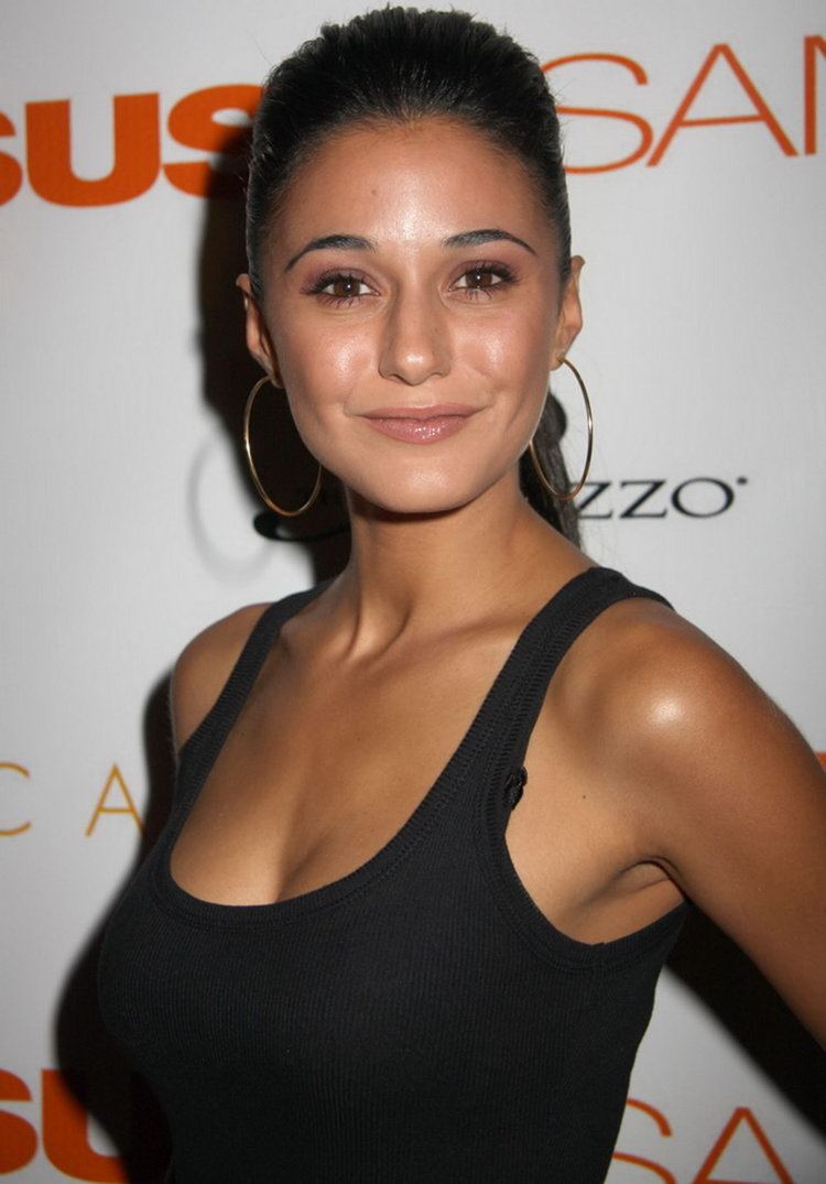 Emmanuelle Chriqui smiling with a ponytail hairstyle and wearing a black knitted sleeveless blouse exposing her cleavage and gold round earrings