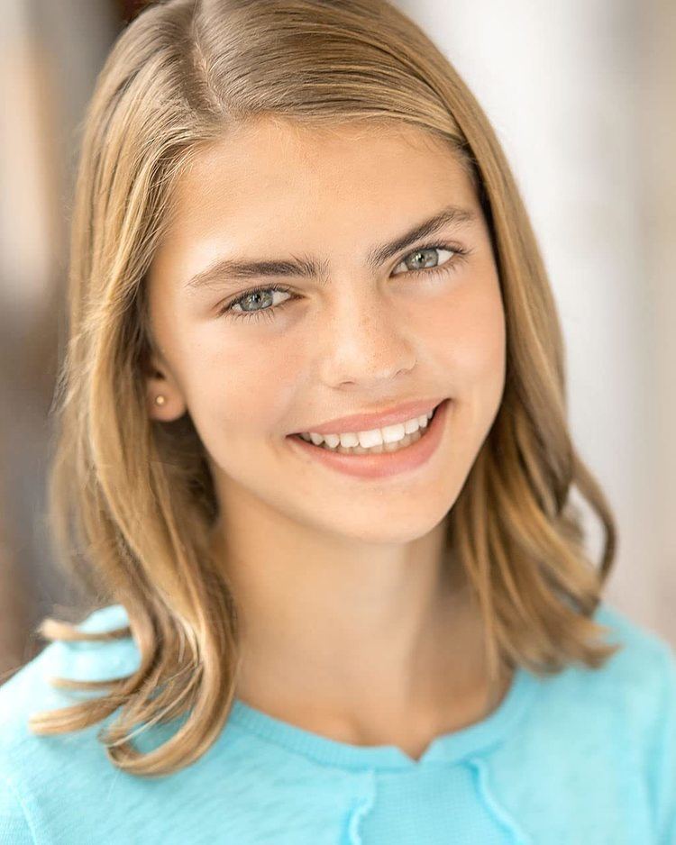 Emmie Hunter smiling with her blonde hair down while wearing a light blue blouse and necklace
