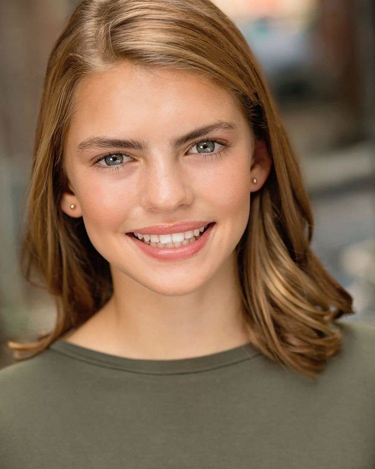 Emmie Hunter smiling with her blonde hair down while wearing a gray blouse and necklace