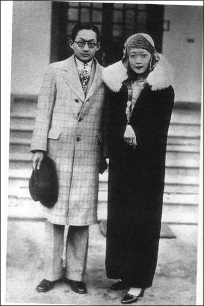 Empress Wanrong and Puyi with serious faces. Empress Wanrong wearing a headscarf and a black fur coat while Puyi wearing eyeglasses and a checkered coat.