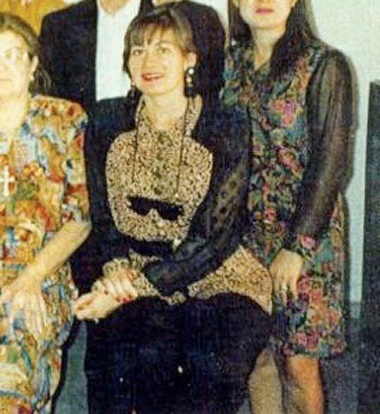 Enedina Arellano Félix smiling with her family while sitting on the chair and wearing a black and brown long sleeve blouse, black pants, earrings, and sunglasses with strap