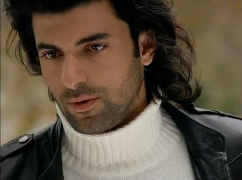 Engin Akyürek wearing a black coat and white turtle-neck shirt