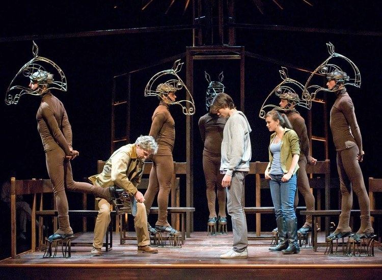 A man fixing the horse's hoof and another man and woman looking at him in a scene from the play Equus