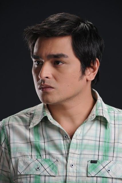 Eric Fructuoso posing while wearing a white checkered buttoned shirt and clean shaven.