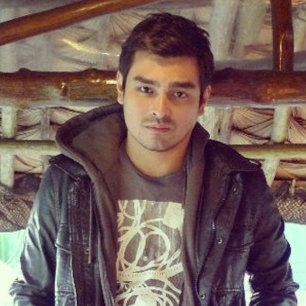 Eric Fructuoso posing inside a hut and wearing a jean jacket over a gray shirt.