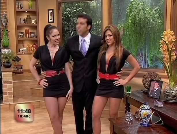 Felipe Viel hosting the Escándalo TV show with two women beside him wearing a black dress and red belt while Felipe is wearing a black coat, white long sleeves, necktie, and pants