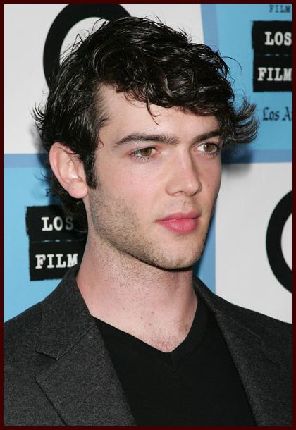 Ethan Peck with pouty lips and has black hair, a beard, and mustache, and wearing a black shirt under a black coat