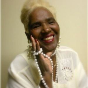 Etterlene DeBarge smiling while holding a pearl necklace and wearing a white dress.